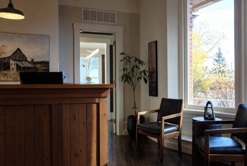 A calm dental reception area with a wooden counter and a tall window letting in daylight