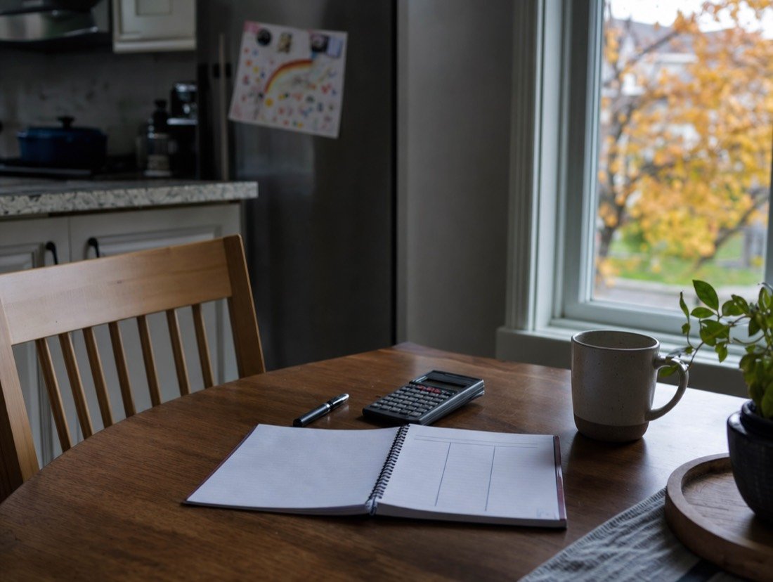 A notebook and calculator laid out on a kitchen table for working through a monthly budget