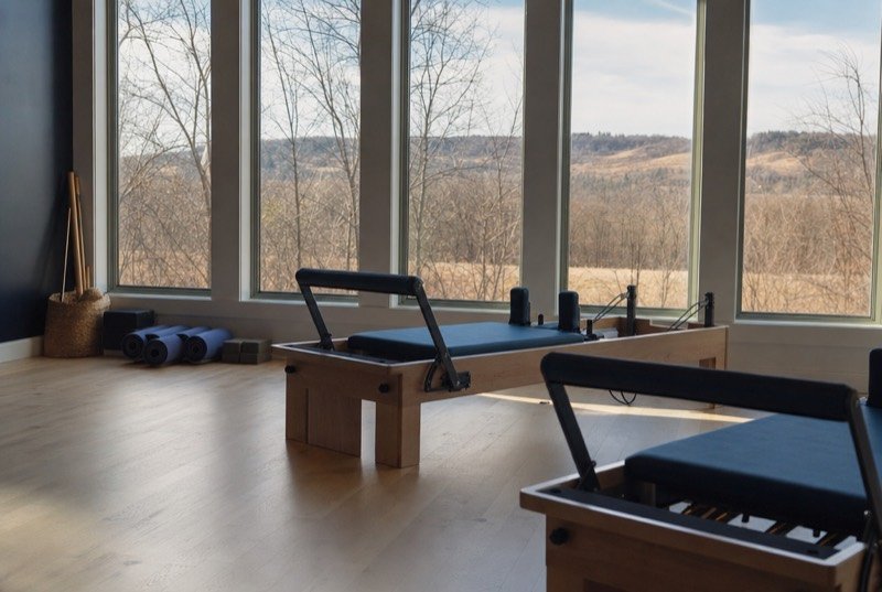 Reformer machines and yoga mats on a pale wooden floor in a studio filled with morning light