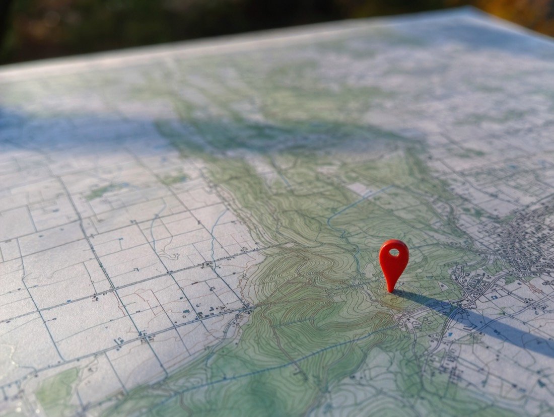 Close-up of a single red map pin stuck in a paper contour map